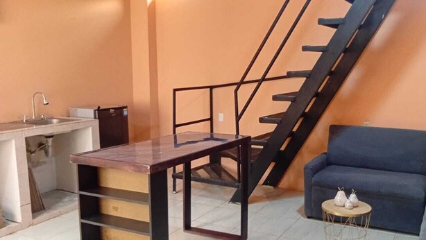 A compact living space with a kitchen area, a sofa, a small round table, and a staircase. - Downtown 2-story Tiny House (Granada)