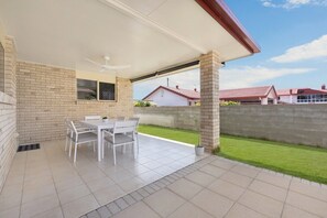 A covered patio area with a table and chairs, a brick wall, and a view of a residential neighborhood. - Sweet Retreat Rosslea (Rosslea)