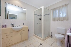 A bathroom with a shower, toilet, sink, and mirror.