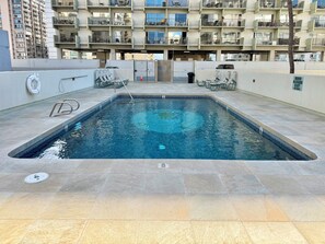 Ein rechteckiger Pool mit gefliestem Sonnendeck, umgeben von einem Hochhaus mit Balkonen.