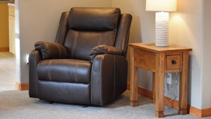 Un fauteuil inclinable en cuir marron, avec une petite table en bois à côté, sur laquelle se trouvent une lampe et un tiroir.