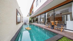 Ein modernes Haus mit Pool, Holzterrasse und großen Glasfenstern.