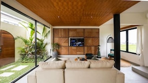 Ein modernes Wohnzimmer mit großem Fernseher, Wandverkleidung aus Holz und Blick auf einen Garten.