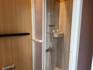 Een douche met een houten wand, een wit plankje met toiletartikelen en een metalen kraan.