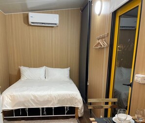Een slaapkamer met een bed, een airconditioner, een kledingkast en een tafel met een stoel.