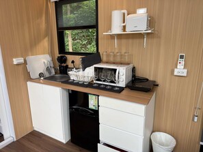 Een kleine keuken met een magnetron, koffiezetapparaat en wijnglazen op het aanrecht.