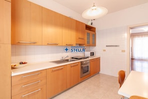 A kitchen with wooden cabinets, a microwave, a sink, and a stove. - Vicolo Grifone *zona centrale*/trilocale# (Jesolo)