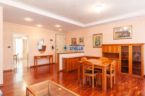 A spacious room with a wooden dining table, chairs, a glass coffee table, a reception desk, and a wooden cabinet. - Vicolo Grifone *zona centrale*/trilocale# (Jesolo)