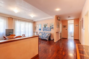 A spacious living area with a wooden floor, a sofa, a dining table with chairs, and a TV. - Vicolo Grifone *zona centrale*/trilocale# (Jesolo)