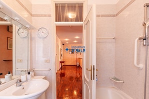 A bathroom with a sink, mirror, clock, and shower. - Vicolo Grifone *zona centrale*/trilocale# (Jesolo)