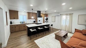 A modern kitchen with a central island, wooden cabinets, and a dining area with bar stools.