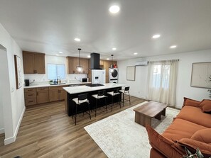 A modern kitchen with a central island, wooden cabinets, and a dining area with bar stools. - 洛杉矶pomona全新装修独立屋｜2房2卫三床（含高低床）｜室内洗烘｜免费停车｜最多4人｜精致原木风 (Pomona)