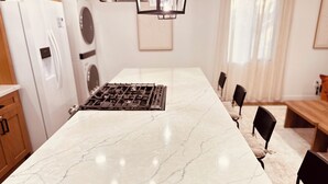 A kitchen with a marble countertop, a gas stove, wooden cabinets, and a dining area with chairs and a bench.