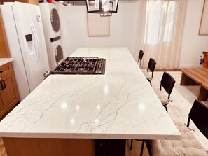 A kitchen with a marble countertop, a gas stove, wooden cabinets, and a dining area with chairs and a bench. - 洛杉矶pomona全新装修独立屋｜2房2卫三床（含高低床）｜室内洗烘｜免费停车｜最多4人｜精致原木风 (Pomona)
