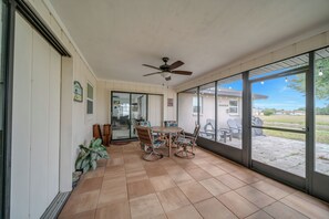 A sunlit patio with a table and chairs, a ceiling fan, and a view of the outdoors.