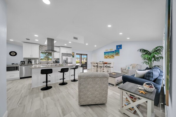 A modern kitchen with white cabinets, a stainless steel range hood, and a dining area with a white table and chairs.