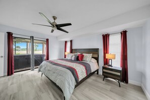 A bedroom with a bed, a nightstand, a ceiling fan, and a view through a sliding door.