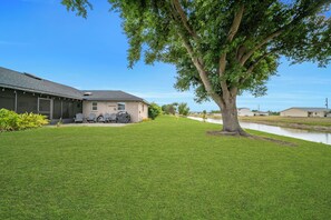 A house with a large lawn, a tree, and a body of water.