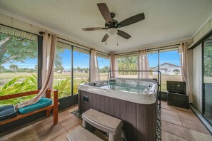 Ein Whirlpool in einem Raum mit großen Fenstern, einem Deckenventilator und einer Sitzbank.