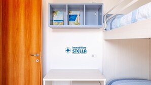 Ett sovrum med en våningssäng, ett skrivbord med en stol, en liten pall och en hylla med tavlor.