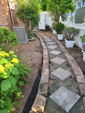 Ein Gartenpfad mit trittfesten Steinen, einer Backsteinmauer und Kübelpflanzen.