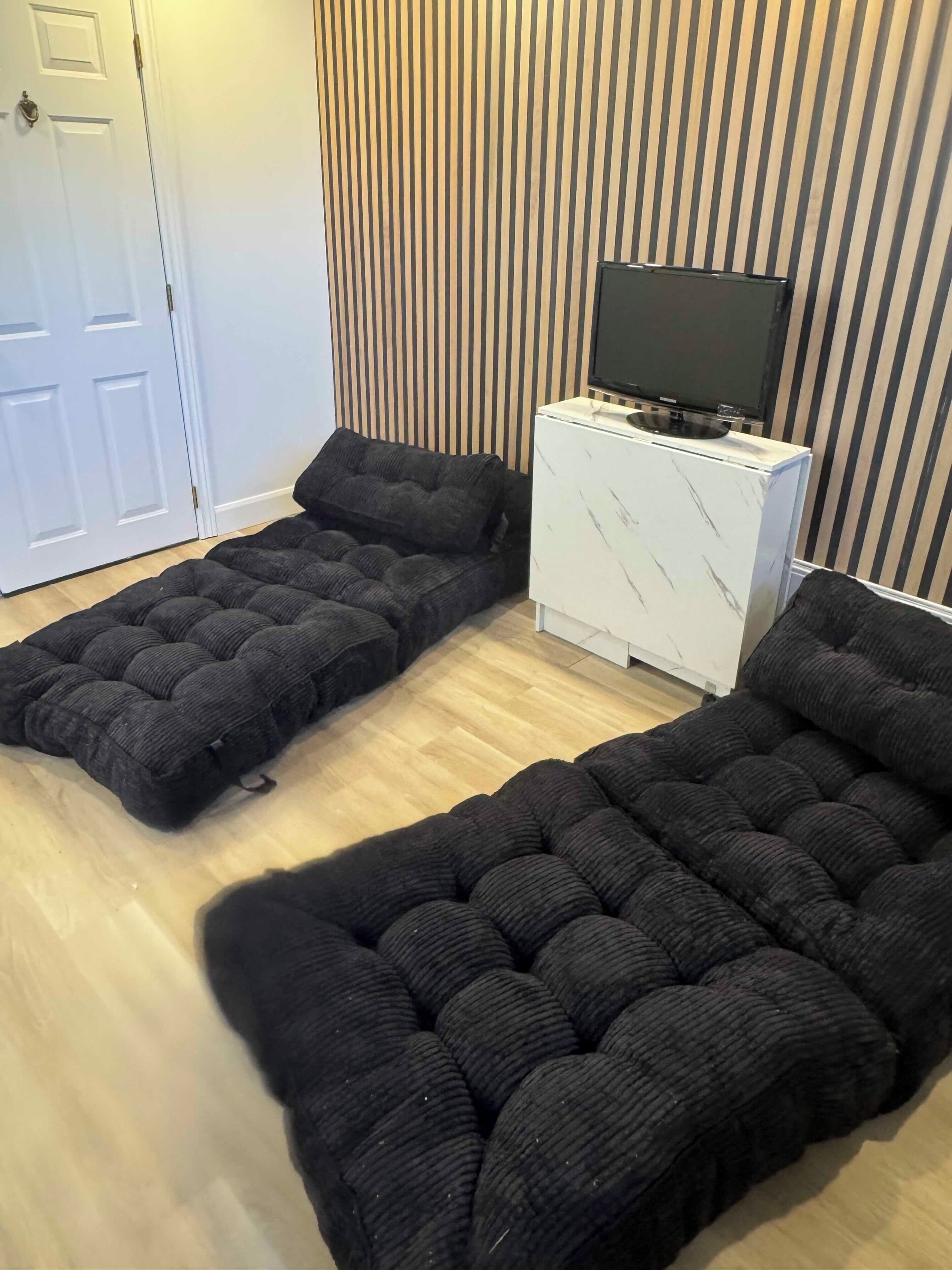 A room with a sofa bed, a television on a cabinet, and a striped wall.