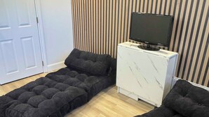 Una habitación con sofá cama, televisor en un mueble y pared a rayas.