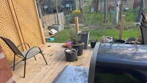 Una terraza de madera con una parrilla, plantas en macetas y una silla.