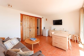 Ein Wohnzimmer mit einer Couch, einem Couchtisch, einem Holzessttisch und einem an der Wand montierten Fernseher.