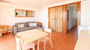 A living room with a sofa, a dining table, and chairs. There is a wooden wardrobe and a mirror on the wall. - 2-room apartment with sea view - A/C, Loggia (PORT GRIMAUD)