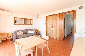 Ein Wohnzimmer mit einer Couch, einem Esstisch und Stühlen. Es gibt einen Holzschrank und einen Spiegel an der Wand.