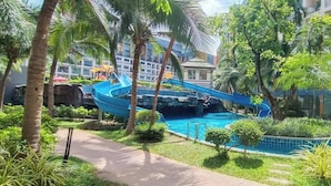 A pool area with a blue water slide, surrounded by palm trees and greenery. - Room-stylish 1BR Garden View at Laguna B (Pattaya)