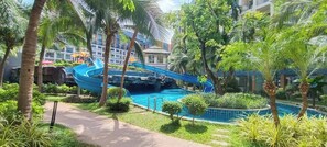 A pool area with a blue water slide, surrounded by palm trees and greenery. - Room-stylish 1BR Garden View at Laguna B (Pattaya)