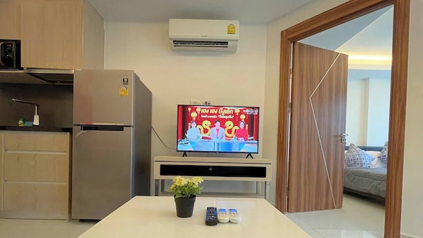 A compact living space with a kitchenette, a flat-screen TV, a small table with a plant, and a door leading to a balcony. - Room-stylish 1BR Garden View at Laguna B (Pattaya)