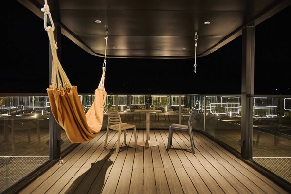 Un balcon extérieur moderne, agrémenté d’un hamac suspendu, d’une table et de chaises.