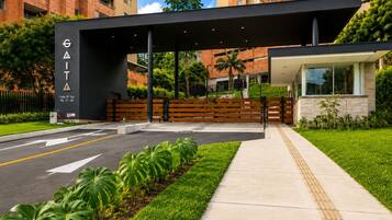 A modern building entrance with a covered walkway, a parking area, and a well-maintained lawn.