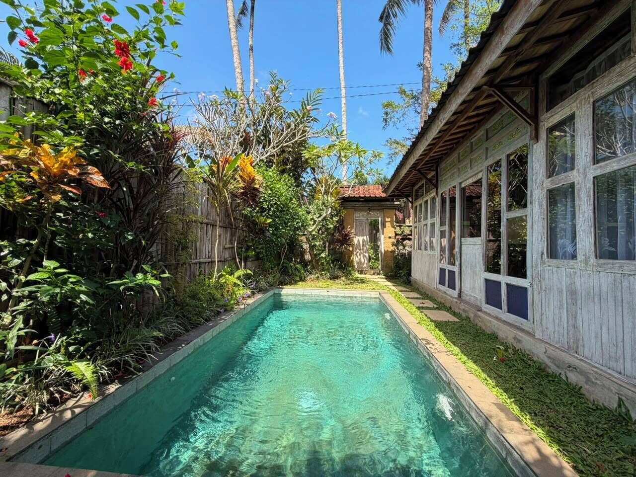 A swimming pool surrounded by lush greenery and a wooden building with large windows.