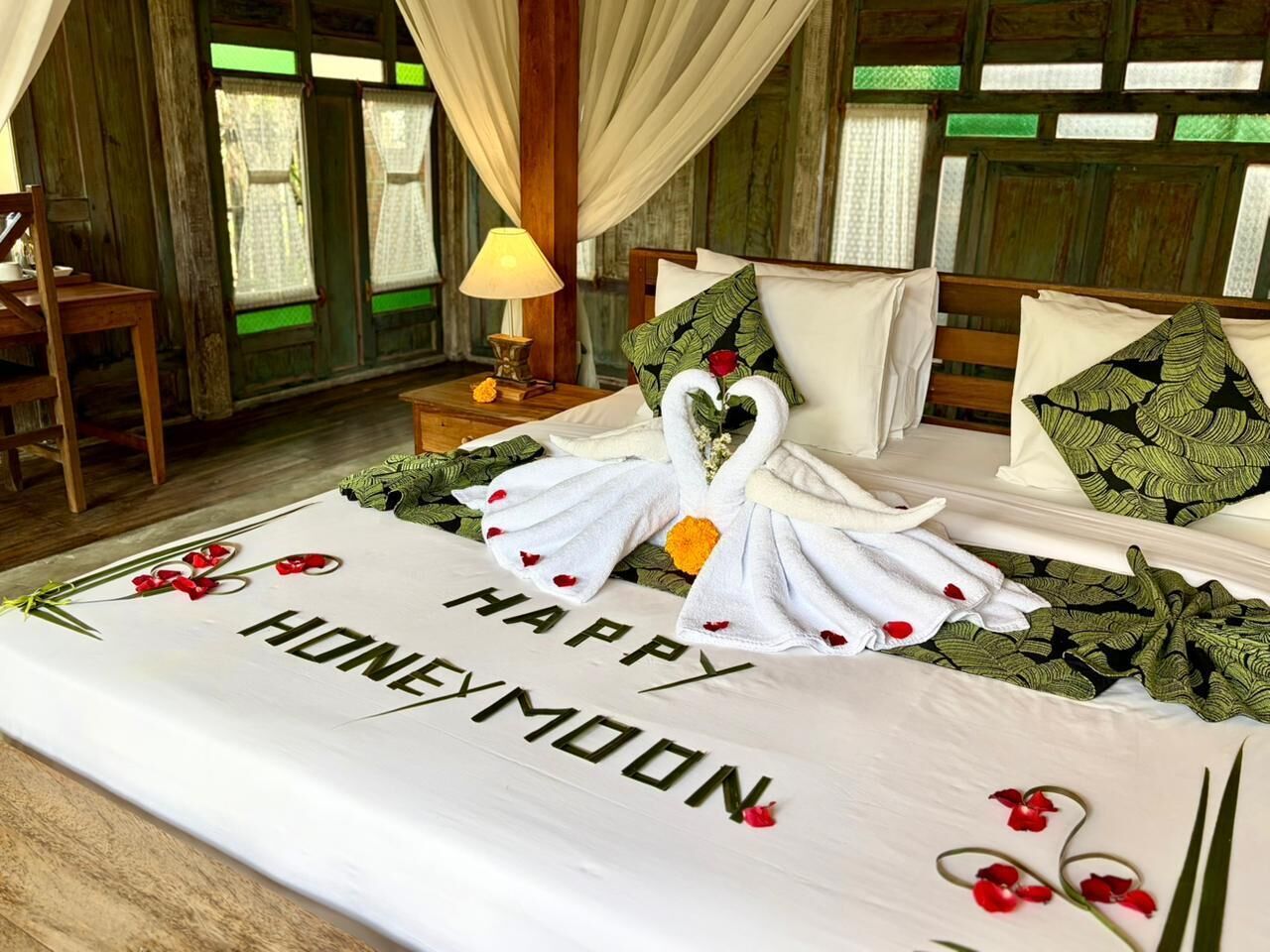 Una cama con un mensaje que dice 'Luna de miel feliz', un ramo de rosas rojas y una decoración con forma de cisne.