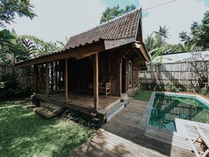 A wooden house with a tiled roof, a wooden deck, and a swimming pool. - Sarini Villas by Manara (Sukawati)