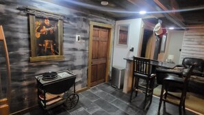 A room with a stone wall, a wooden door, a small table, a chair, and a grill cart.