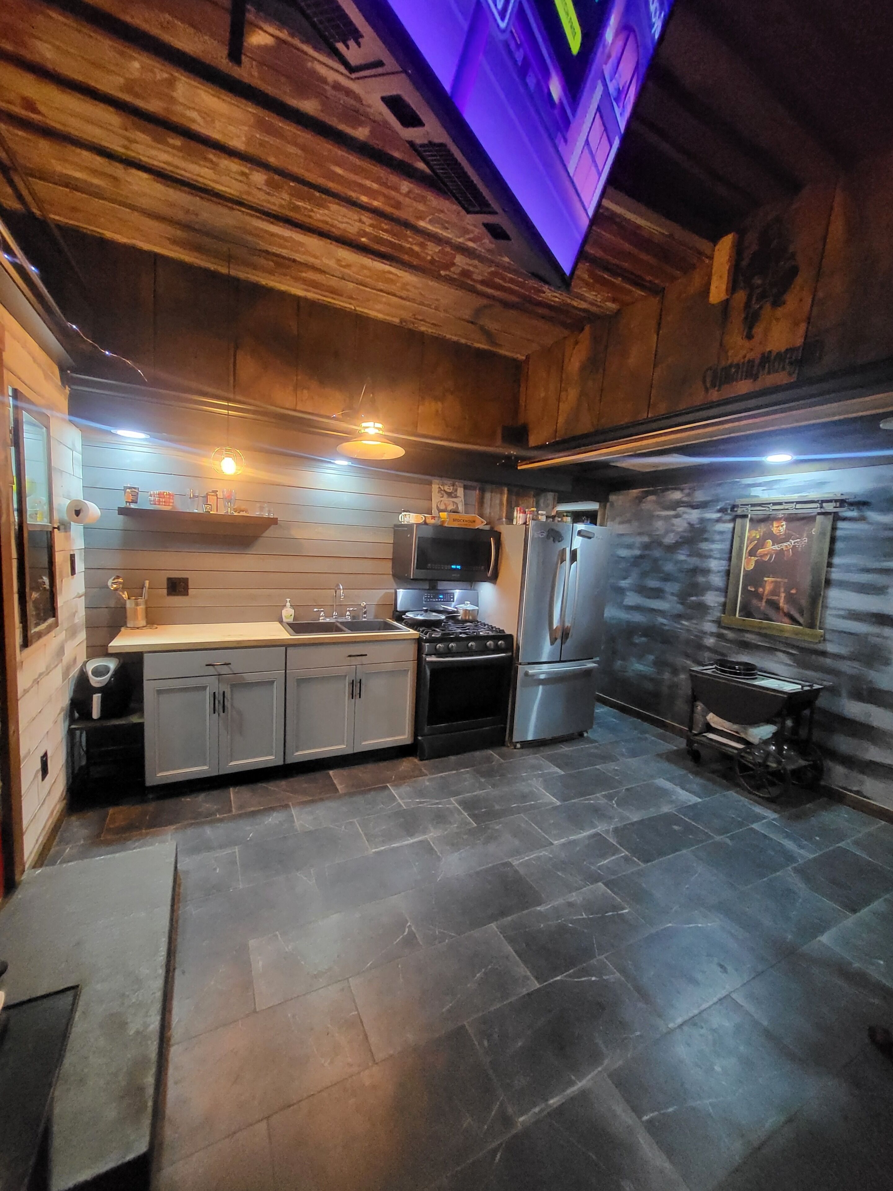 A kitchen with a wooden ceiling, a microwave, a stove, and a refrigerator.
