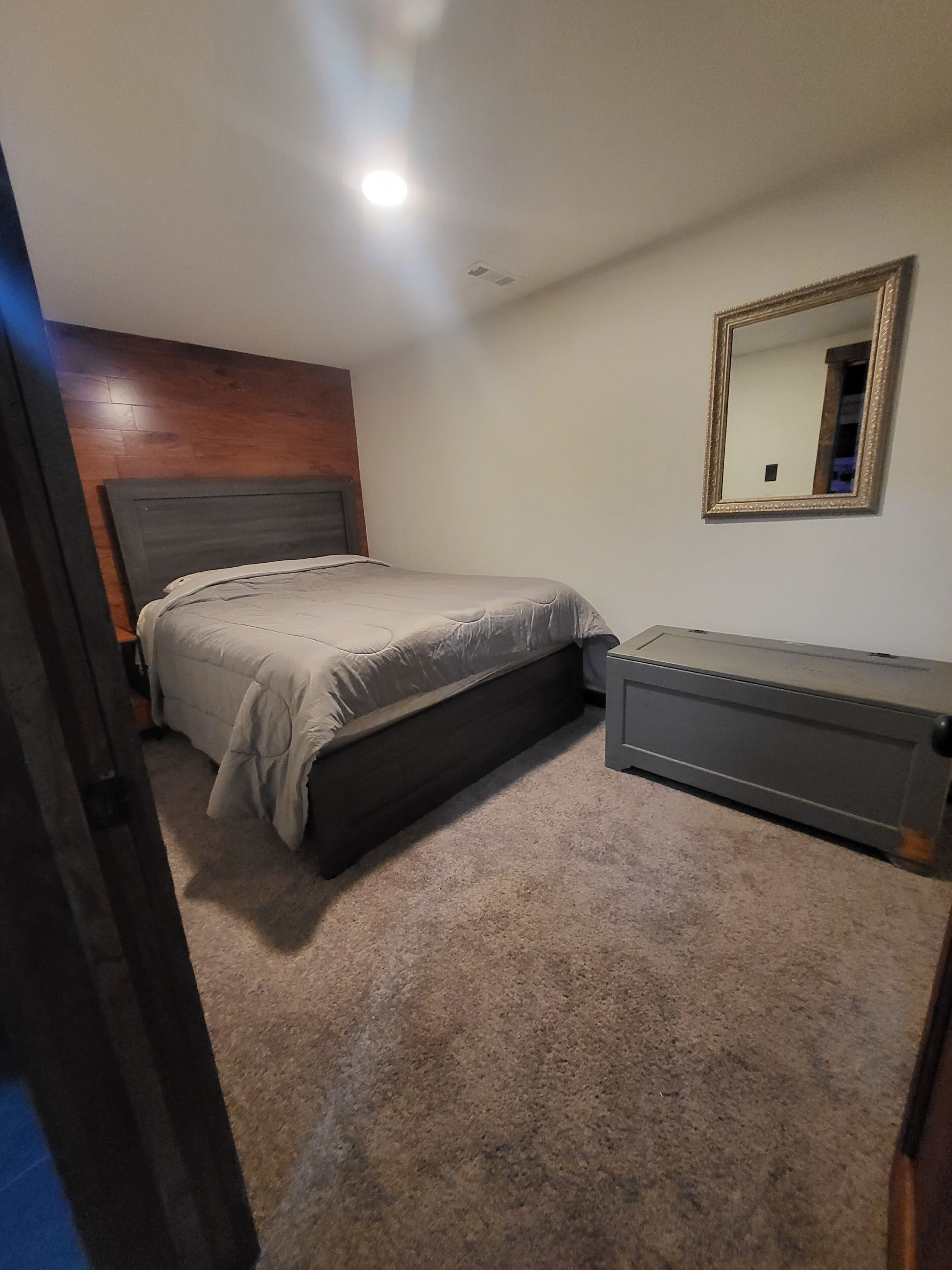 Une chambre à coucher avec un lit, une commode, un miroir et une tête de lit en bois.
