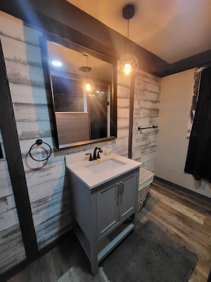 Une salle de bain avec un lavabo blanc, des meubles sombres, un miroir et un mur en bois.