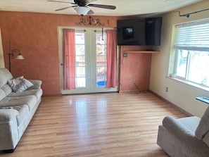 A living room with a sofa, a chair, a ceiling fan, a TV, and a sliding glass door with curtains.
