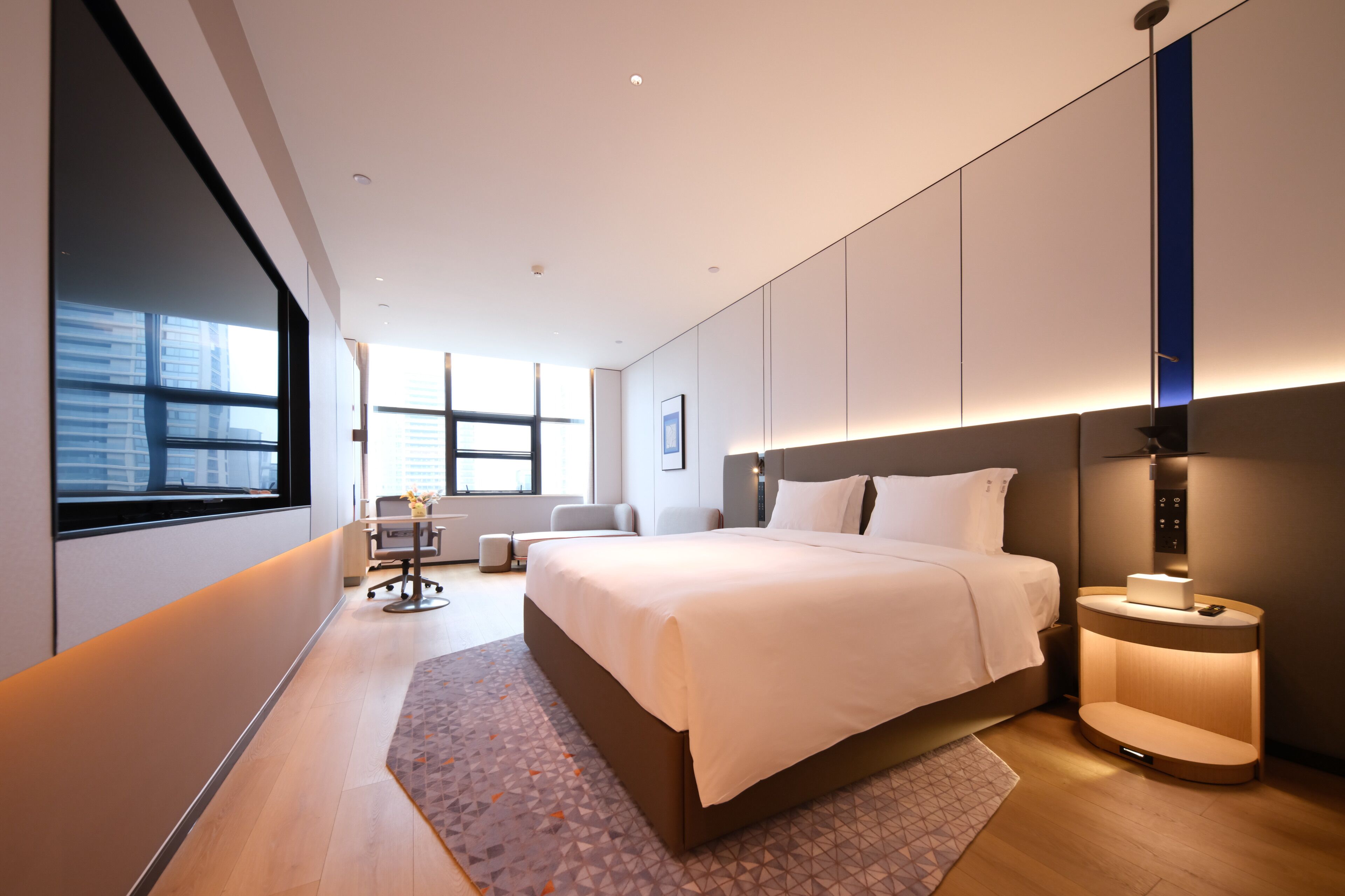 Et moderne hotelværelse med en stor seng, natbord og et vindue med udsigt over byen.
