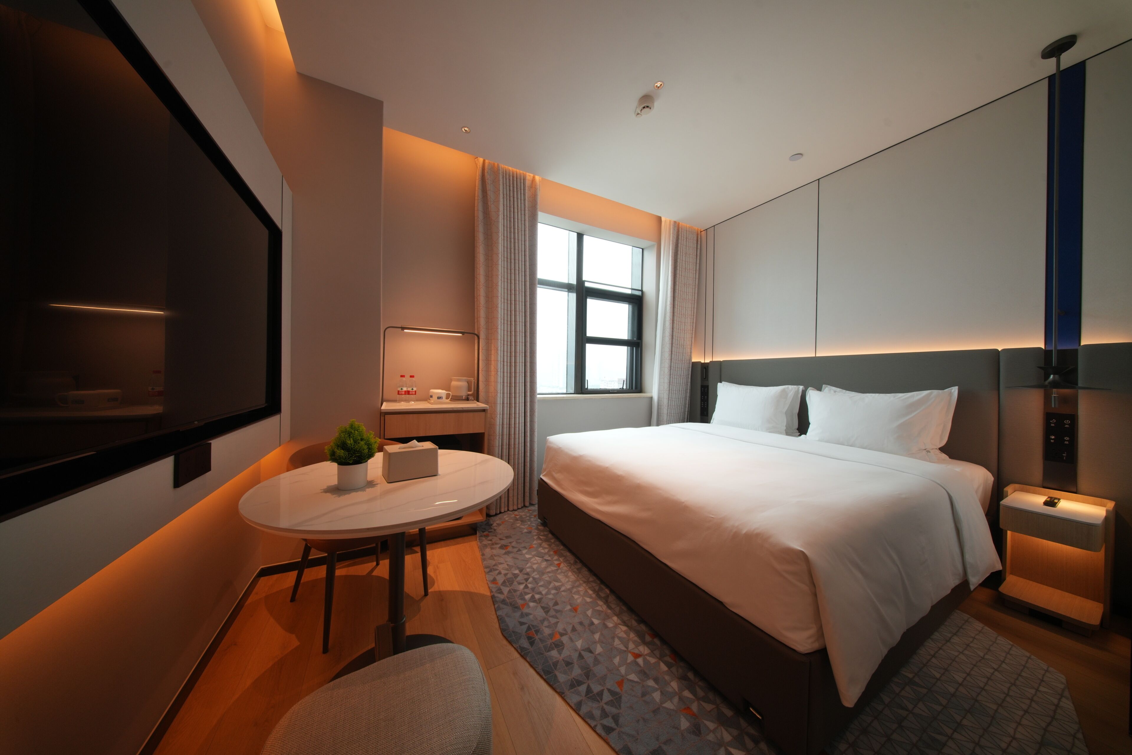 Et moderne hotelværelse med seng, skrivebord, stol, fjernsyn og et vindue.