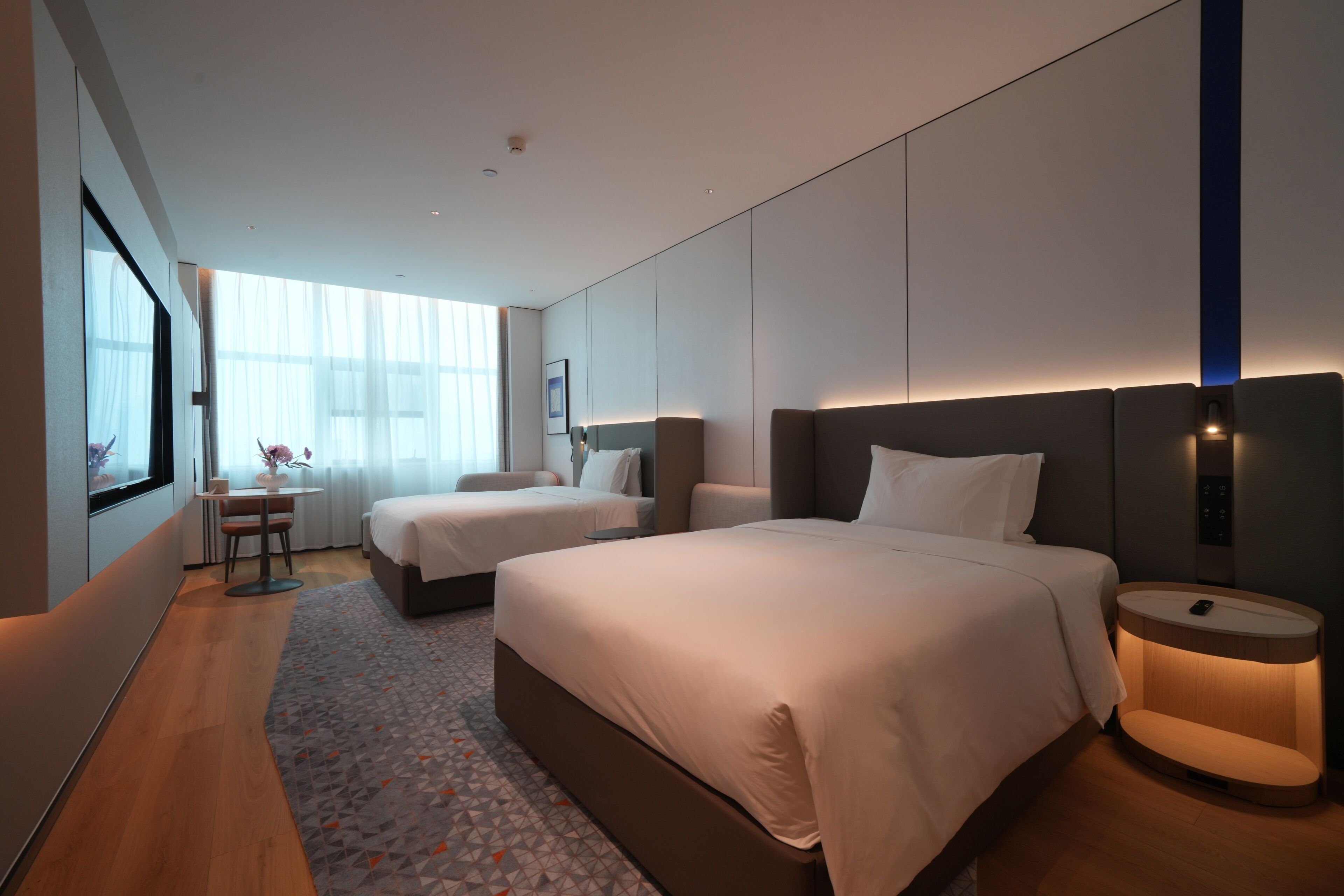 Et moderne hotelværelse med to senge, et skrivebord og et stort vindue.