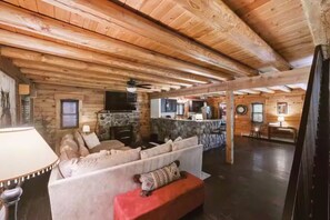 Ein rustikales Blockhaus-Interieur mit Kamin aus Naturstein, Holzbalkendecke, einer Couch und einem Essbereich.