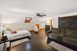 Ein Schlafzimmer mit Bett, Deckenventilator, Schreibtisch, Stuhl, einer Couch und einem Holzschrank.