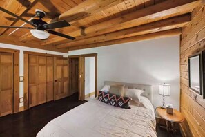 Ein Schlafzimmer mit einem Bett, einem Nachttisch, einer Lampe, einem Deckenventilator und Holzwänden.